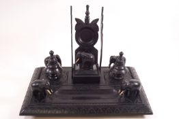 An Indian ebony desk stand carved with elephants and incorporating a pocket watch holder,