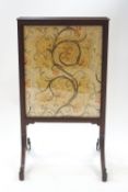 An Edwardian mahogany fire screen, silkwork panel of scrolling foliage to one side,