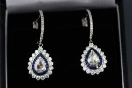 A white metal pair of sapphire and diamond drop earrings centrally set with pear shape rose cut