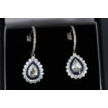 A white metal pair of sapphire and diamond drop earrings centrally set with pear shape rose cut