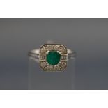 A white metal emerald and diamond cluster ring, centrally set with a square step cut emerald,