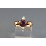 A yellow and rose metal dress ring set with a rhodolite garnet and two seed pearls.