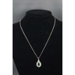 A white metal cluster pendant centrally set with a pear faceted cut emerald, estimated to weigh 1.