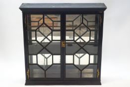 A Victorian ebonised display cabinet with astragal glazed cupboard doors enclosing two shelves and