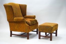 A 20th century wing back armchair with paisley style fabric and matching footstool on reeded legs