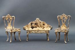 A silver miniature salon suite, comprising of a pair of chairs and a sofa with embossed decoration,