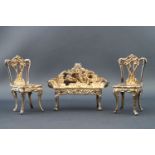 A silver miniature salon suite, comprising of a pair of chairs and a sofa with embossed decoration,