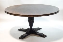 A round oak dining table with carved baluster support and 'X' base,