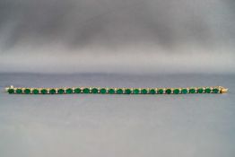 A yellow metal emerald and diamond line bracelet, push in clasp with figure of eight safety catch.