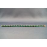 A yellow metal emerald and diamond line bracelet, push in clasp with figure of eight safety catch.