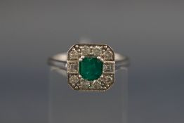 A white metal emerald and diamond cluster ring, centrally set with a square step cut emerald,