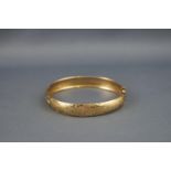A yellow metal hinged bangle with engraved scroll design.