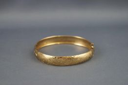 A yellow metal hinged bangle with engraved scroll design.