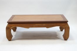 A modern rectangular teak coffee table with shaped apron and inward facing carved legs,