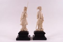 A pair of early 20th century carved ivory figures, one holding an umbrella, the other with a staff,