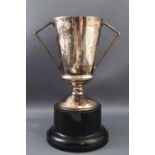 A silver trophy cup, with two angular handles, attached to a simulated ebony plinth, 18.