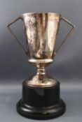 A silver trophy cup, with two angular handles, attached to a simulated ebony plinth, 18.