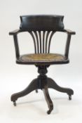 A 1940's stained oak office swivel chair with leatherette seat and brass casters