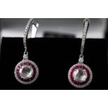 A white metal pair of ruby and diamond drop earrings. Having a central rose cut diamond measuring 6.