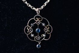 A yellow metal Edwardian pendant set with sapphire and seed pearls suspended from a belcher link
