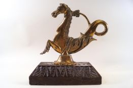 A brass doorstop in the form of a mythical sea creature on a carved wooden base,