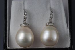 A white metal pair of drop earrings each having a peardrop South Sea pearl (13.