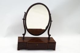 A mahogany oval swing frame mirror on breakfast box base with three drawers on ogee bracket feet,