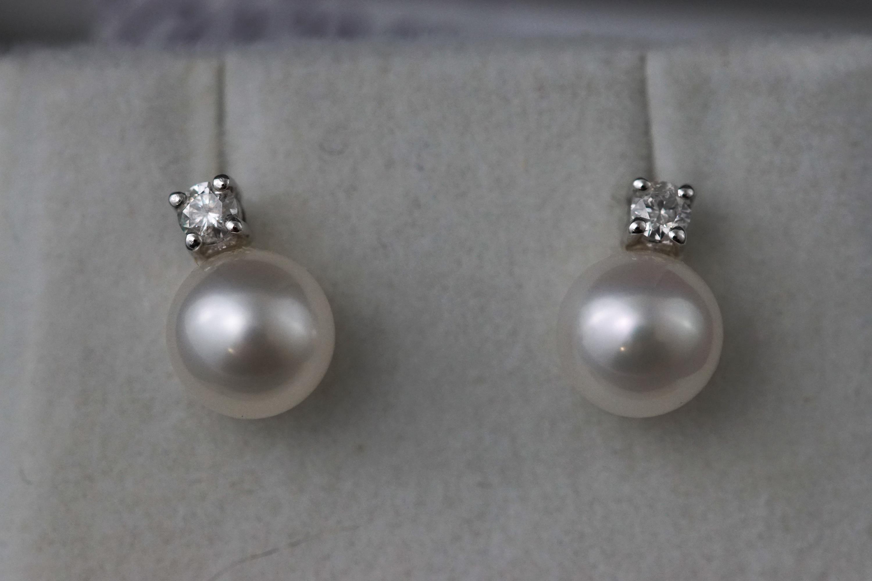 A white metal two stone pair of cultured pearl and diamond stud earrings.