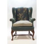 A 18th century style wing armchair raised on carved mahogany cabriole legs united by a stretcher