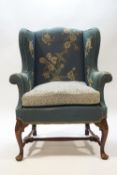 A 18th century style wing armchair raised on carved mahogany cabriole legs united by a stretcher