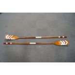 A pair of wooden rowing oars, the blades decorated with white and red chevrons,