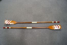 A pair of wooden rowing oars, the blades decorated with white and red chevrons,