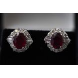 A white metal pair of cluster stud earrings each set with an oval faceted composite ruby.