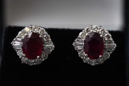 A white metal pair of cluster stud earrings each set with an oval faceted composite ruby.