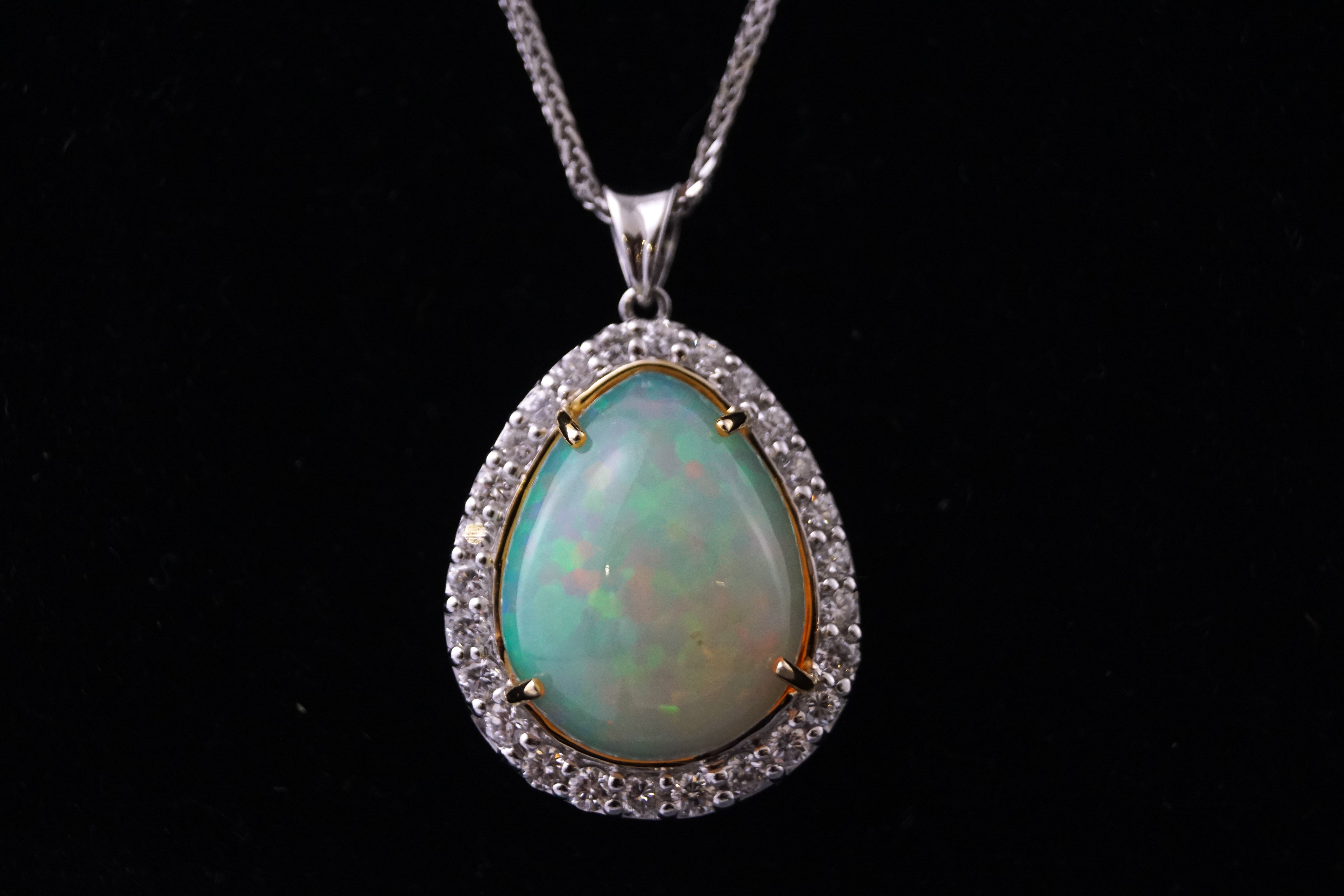 A white metal opal and diamond cluster pendant. Having a pear cut cabochon opal.