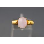 A yellow metal single stone ring set with an oval cabochon cut rose quartz.