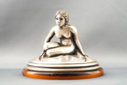 An Italian white metal desk weight, modelled as a seated naked lady, on a faux tortoiseshell base,