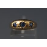 A yellow metal three stone gypsy set sapphire ring. Hallmarked 9ct gold, Birmingham. Size: P.