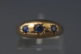 A yellow metal three stone gypsy set sapphire ring. Hallmarked 9ct gold, Birmingham. Size: P.