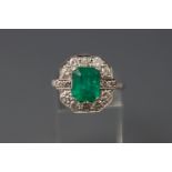 A white metal cluster ring set with a rectangular cut emerald.