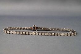 A white metal diamond line bracelet set with fifty round brilliant cut diamonds.