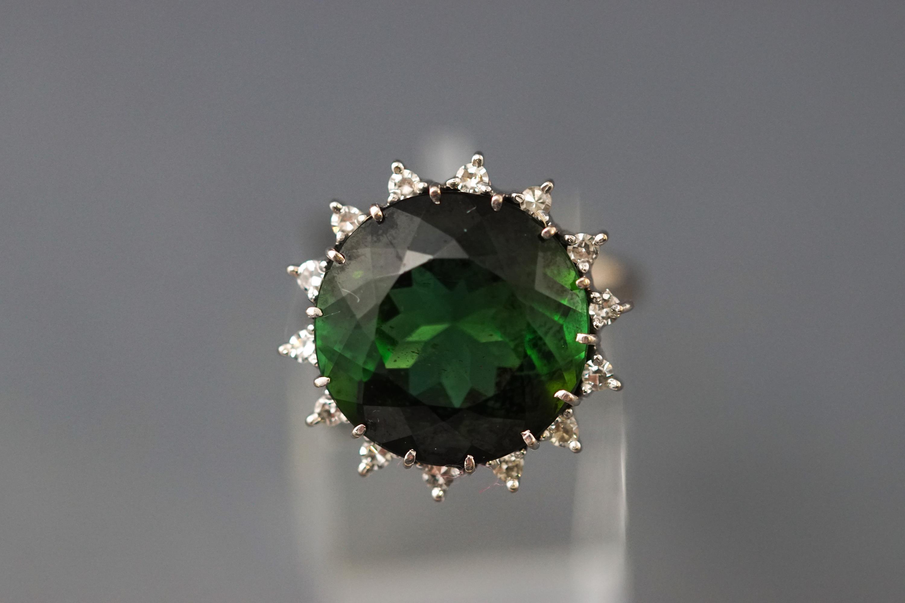 A white metal cluster ring set with a round faceted green tourmaline.