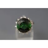 A white metal cluster ring set with a round faceted green tourmaline.