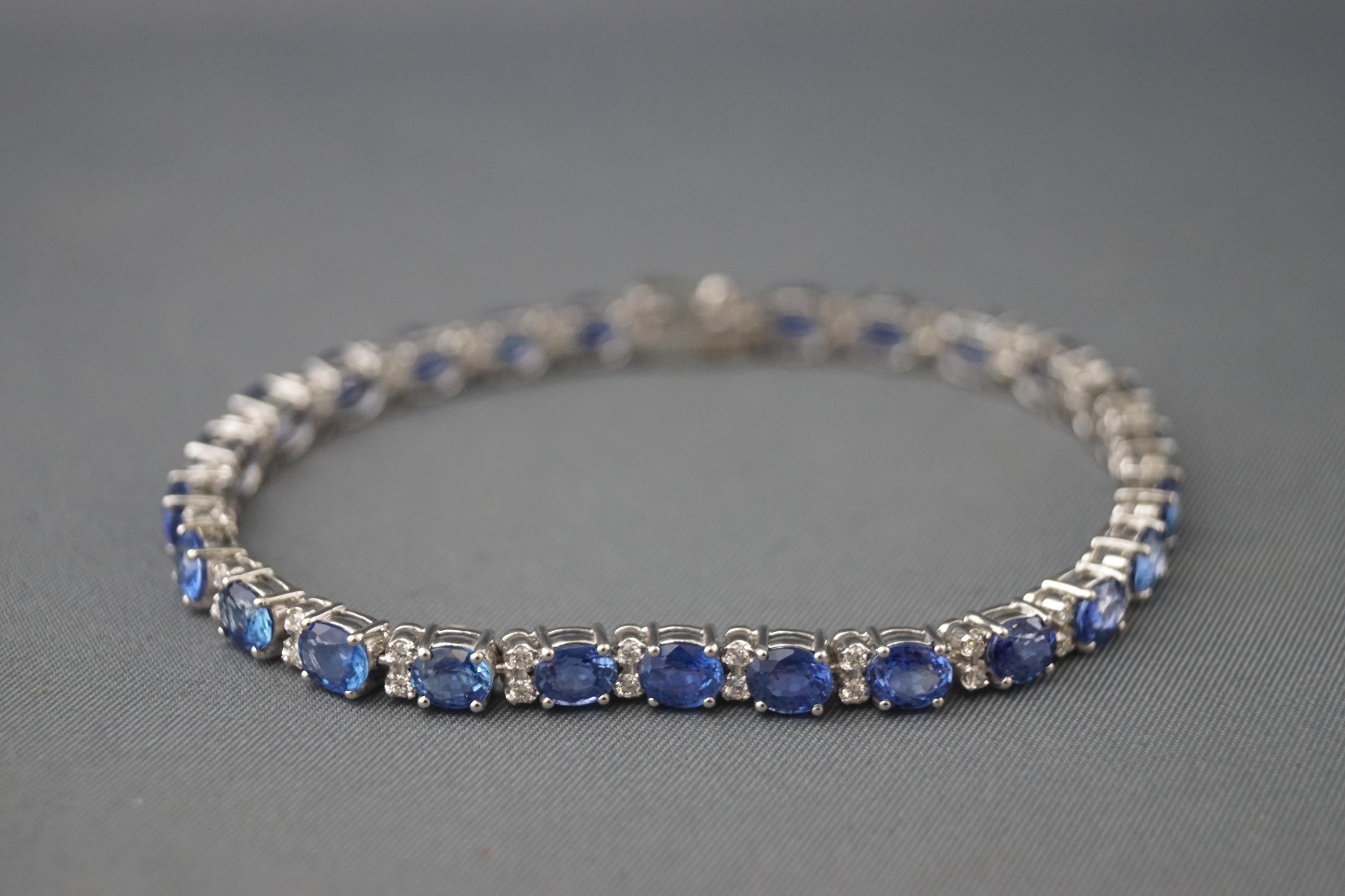 A white metal line bracelet set with oval faceted blue sapphires.