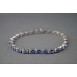 A white metal line bracelet set with oval faceted blue sapphires.