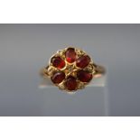 A yellow metal floral cluster ring set with garnets and single cut diamonds.