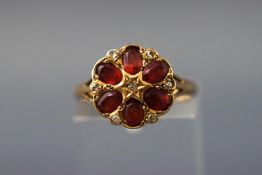 A yellow metal floral cluster ring set with garnets and single cut diamonds.