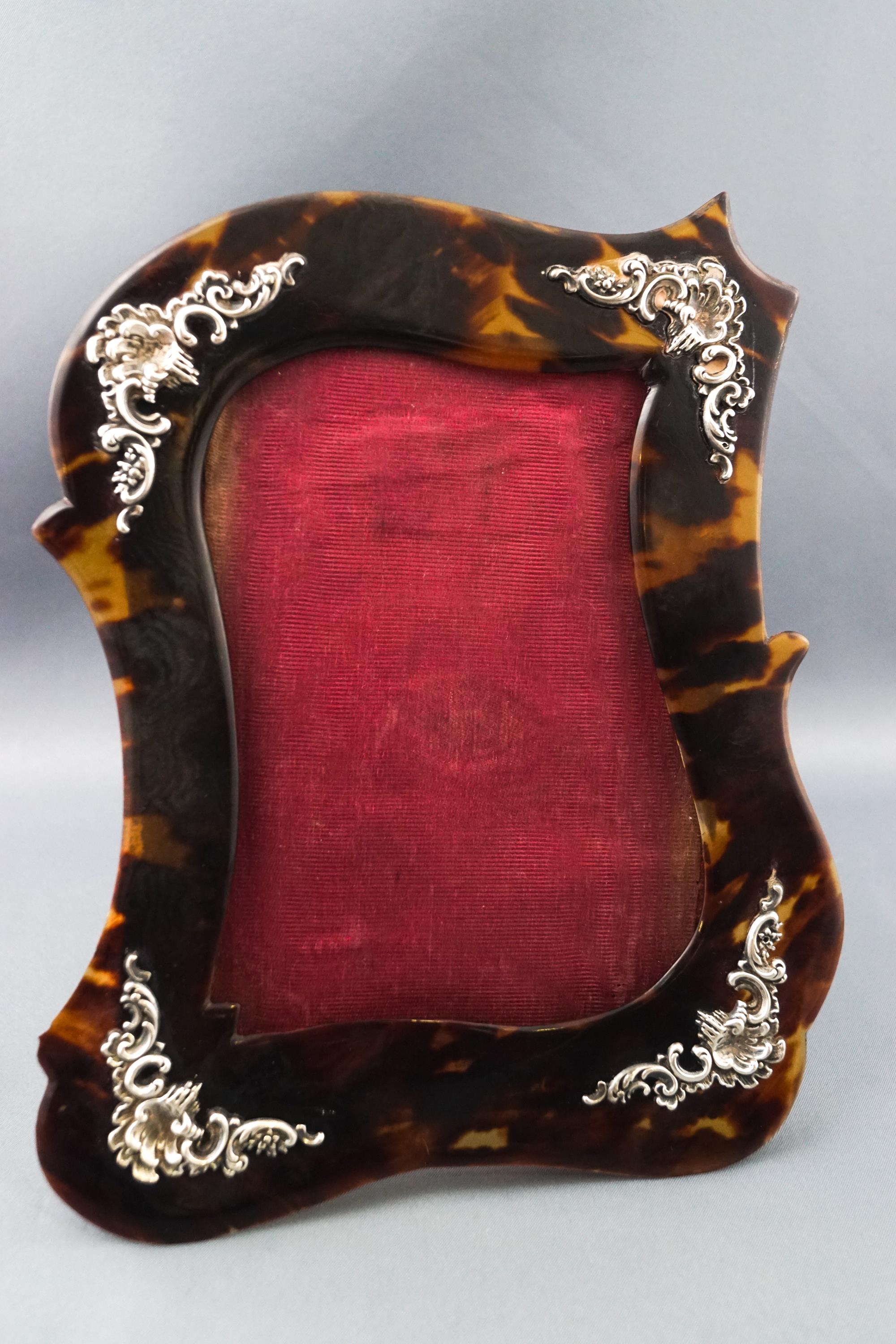 A white metal and tortoiseshell photograph frame of contrived scroll form,