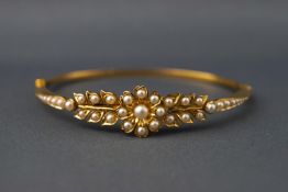 A yellow metal hinged bangle set with seed pearls in a floral and leaf design.