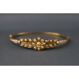 A yellow metal hinged bangle set with seed pearls in a floral and leaf design.